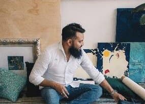 Cristian Armenta sentado en su taller, con obras apoyadas en la pared